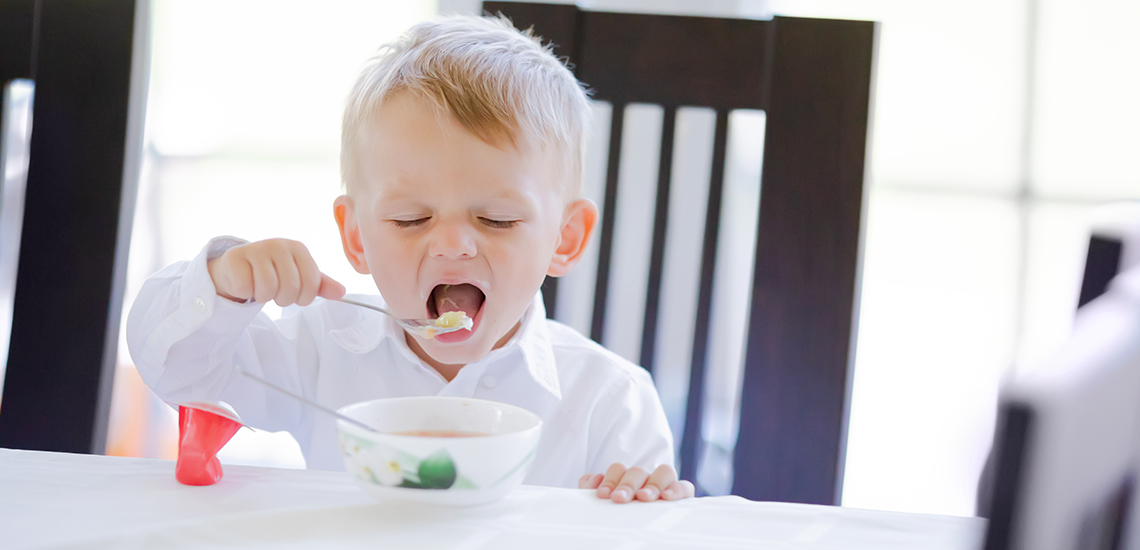En liten gutt sitter og spiser fisk ved middagsbordet.